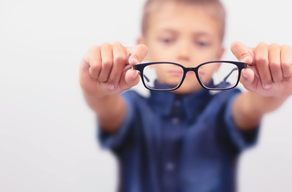 A boy holding a pair of prescription glasses in front of him