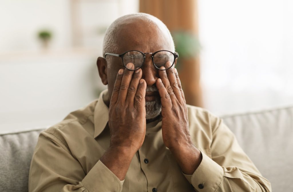 An older man putting his hands over his eyes, underneath his glasses