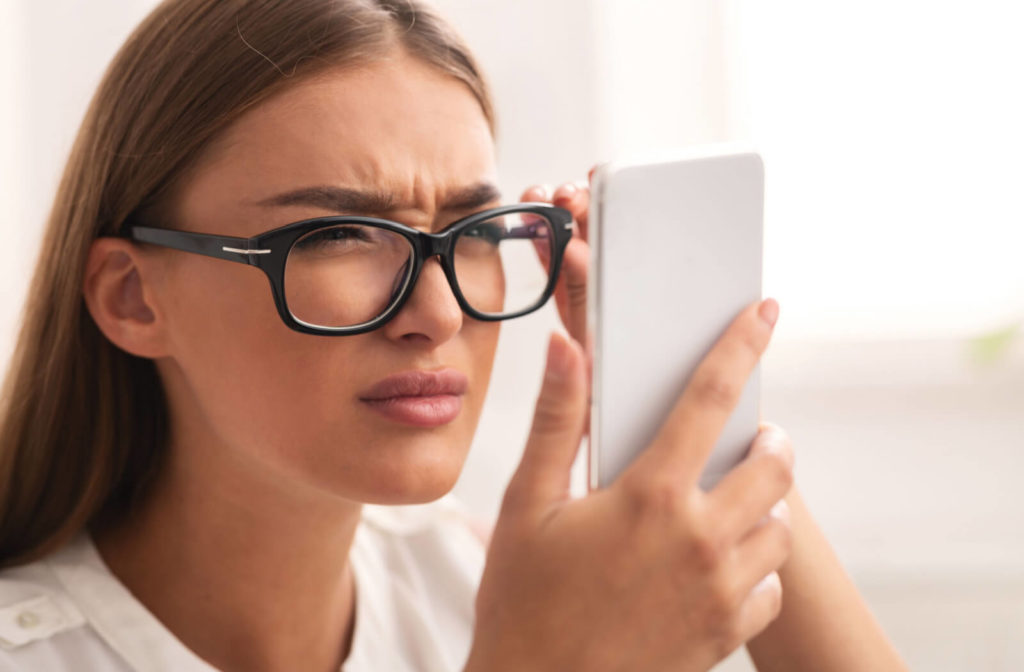 A woman with Myopia or nearsightedness is holding her phone close to her face while wearing eyeglasses