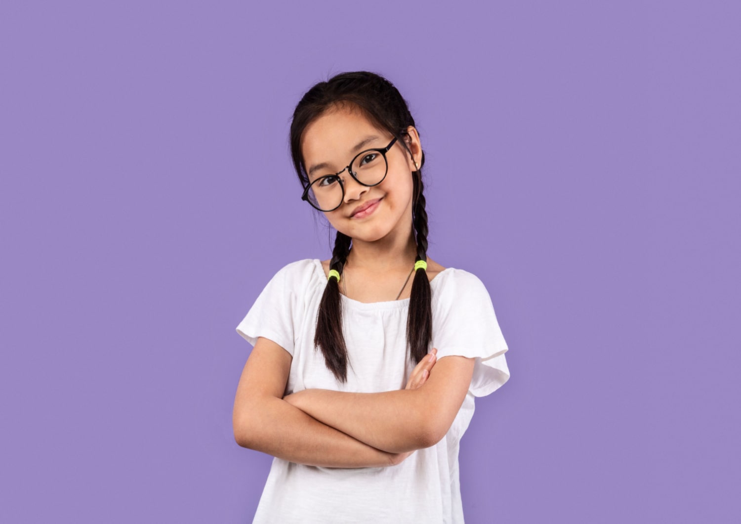 A young girl standing in front of a purple backdrop, crossing her arms. She's wearing glasses to control myopia