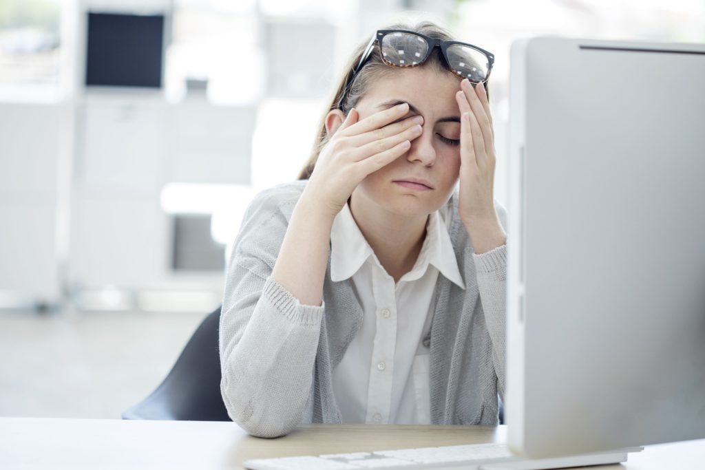 a young woman rubbing her eyes due to eye strain from her computer