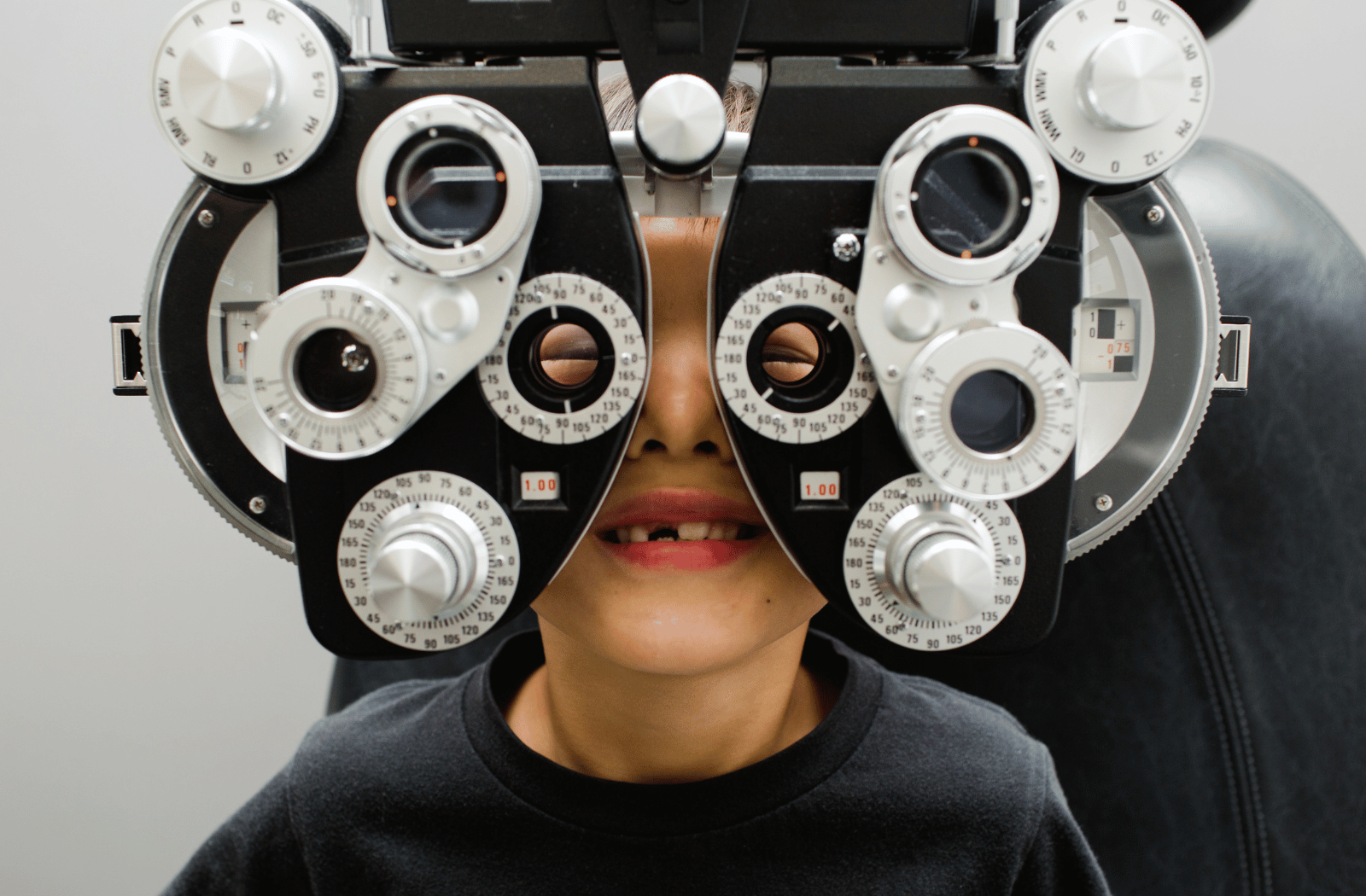 A young boy sitting behind a phoropter at the optometrists office.
