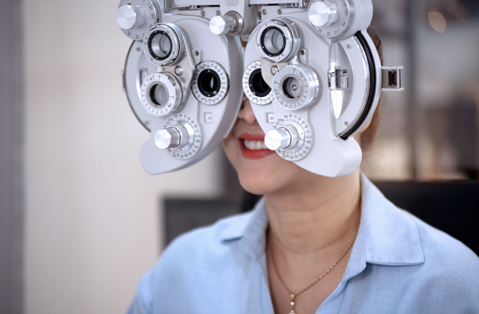 A female patient sits behind a phoropter at the optometrist's office during her eye exam
