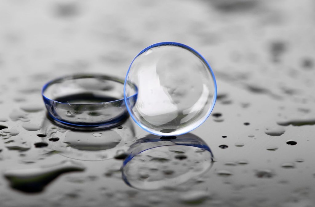 A pair of contact lenses surrounded by droplets of cleaning solution.
