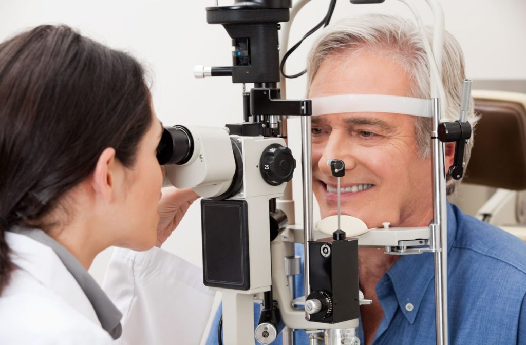 A female optometrist using a medical device to examine the eyes of a older adult man and look for potential eye problems.