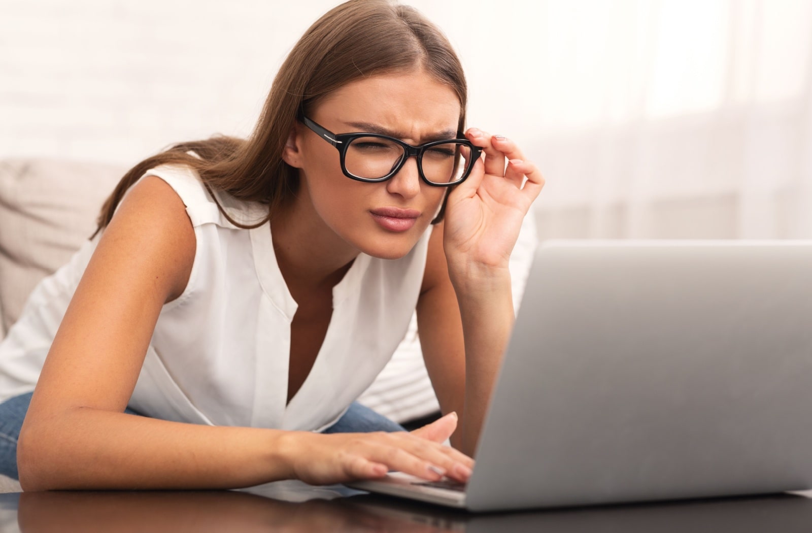 A woman with glasses looking at her laptop but she's struggling to see it clearly due to vision issues