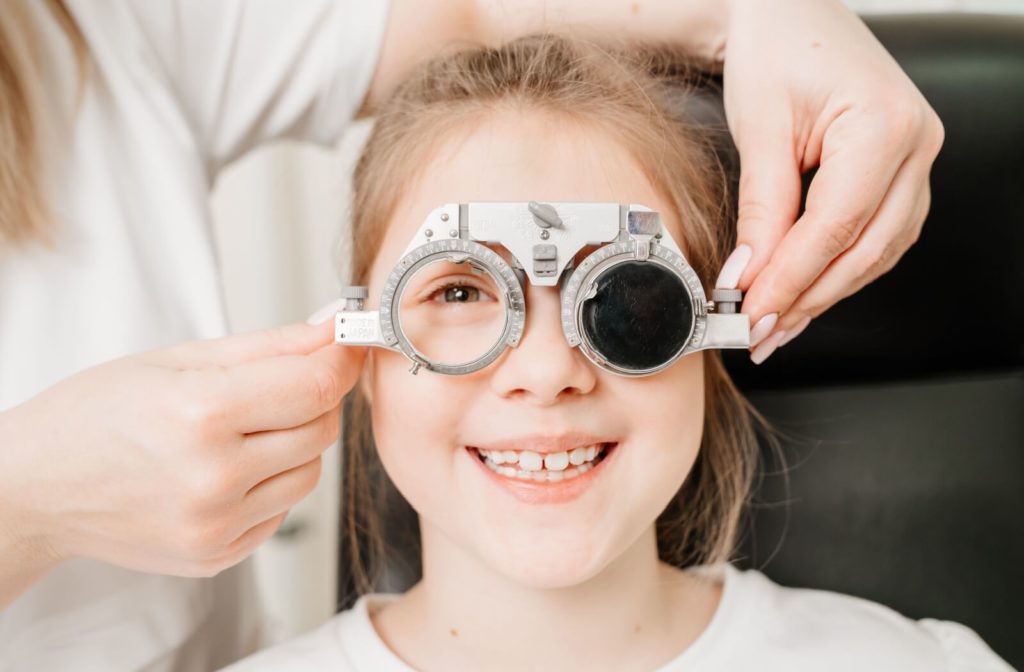 A child smiling while an optometrist holds optical trial frames to the child's face to test her vision.