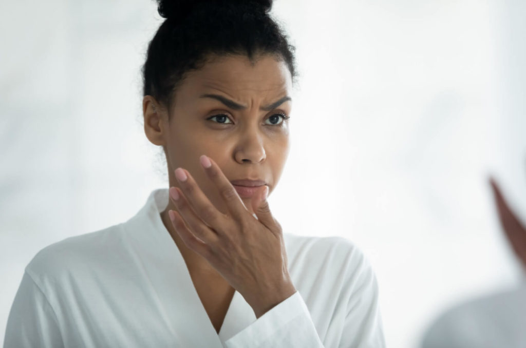 A woman looking at the mirror in the morning raises her left hand to rub her dry eyes.