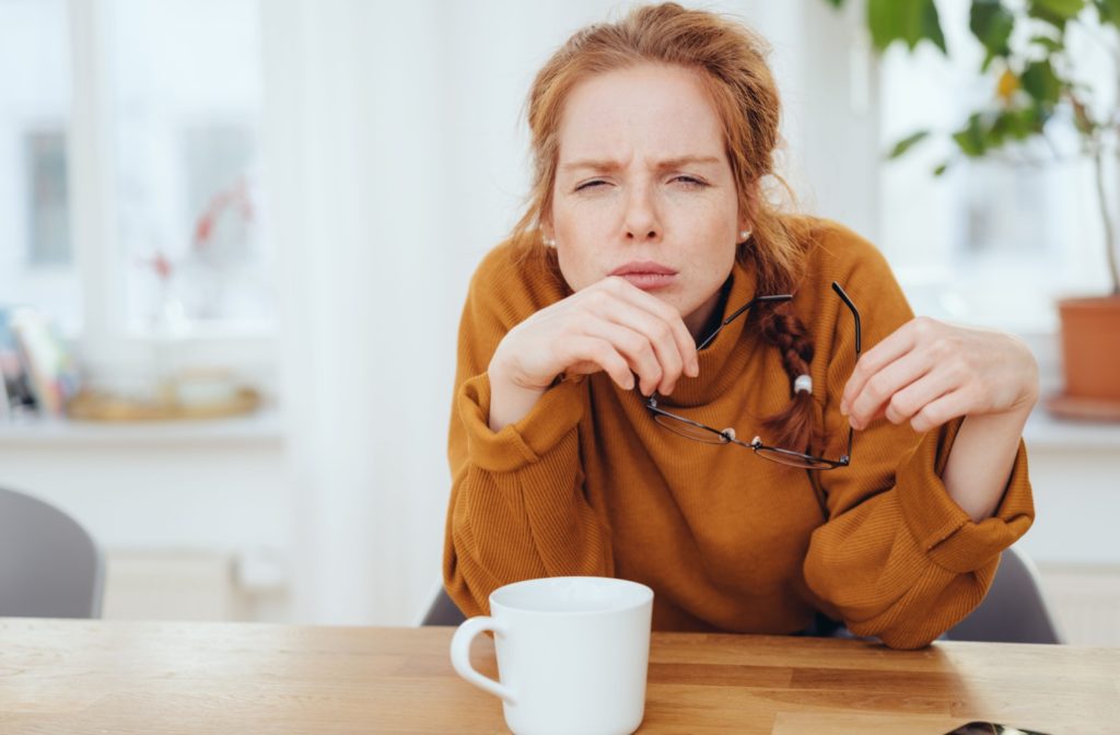 A person trying to improve their visual clarity by squinting their eyes while holding their glasses.