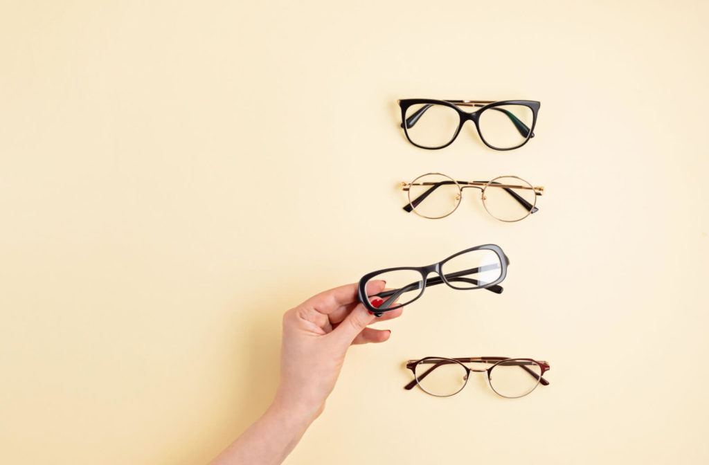 Hand holding eyeglasses with other frames on a beige background.