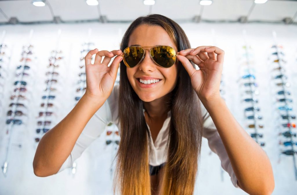 A person cheerfully trying on aviator sunglasses that enhance their heart-shaped face.