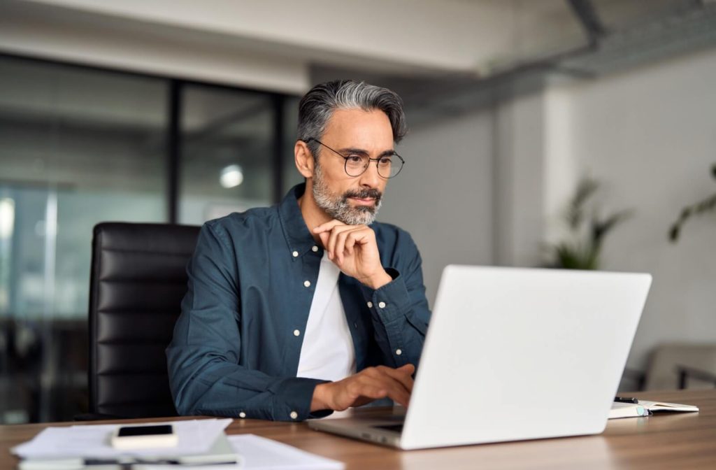 An office worker wearing computer glasses comfortably works on their laptop.